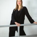 a woman in a black suit leaning on a rail